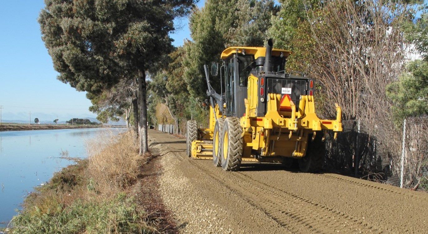 construction vehicle [get the correct type of vehicle] moving along a dirt road next to a river 